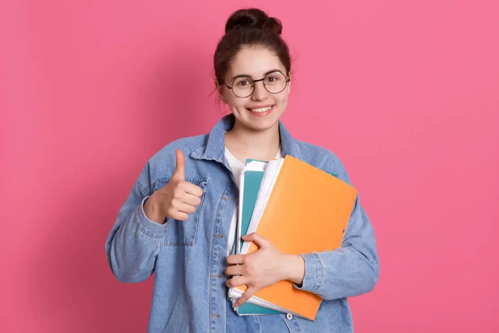 Student with top IELTS band score, smiling and giving a thumbs up while holding folders