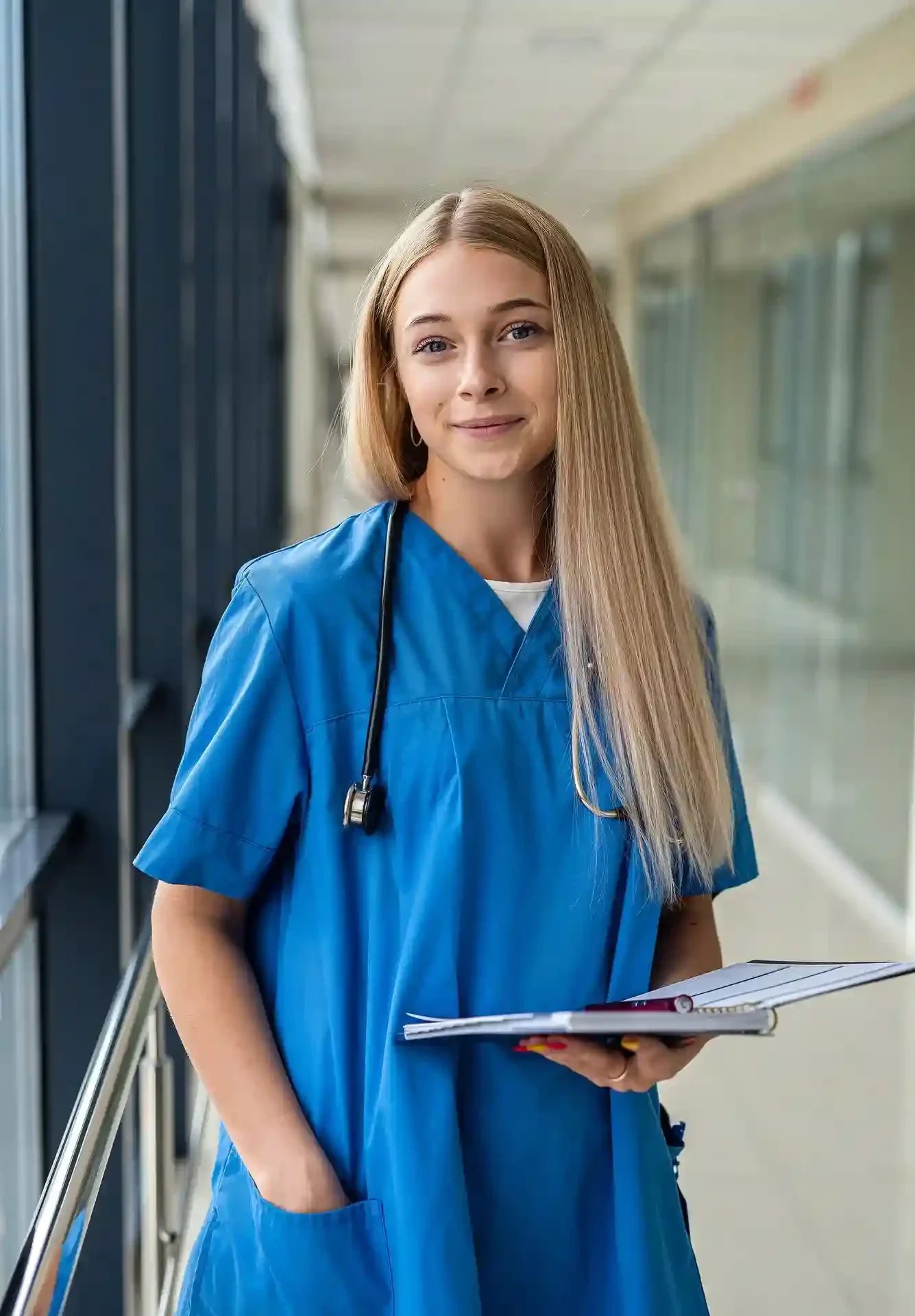 A smiling student in blue scrubs holding a notebook, representing the success of OET coaching in Trivandrum