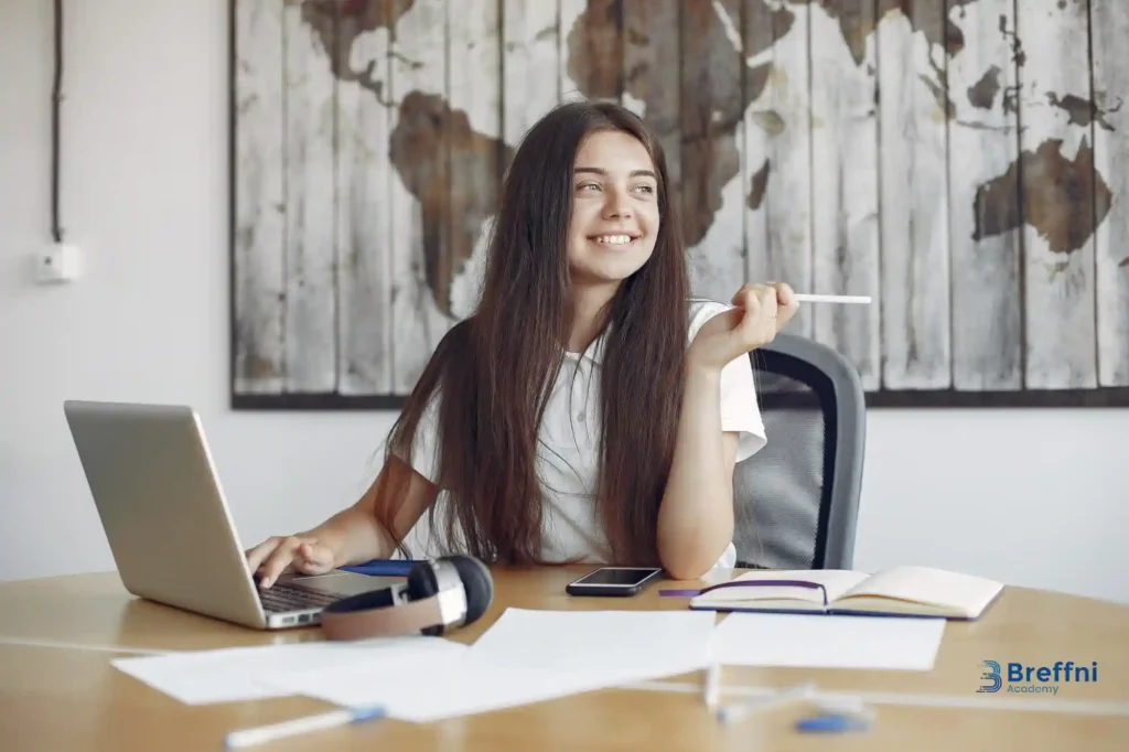 A young woman studying at a desk with a laptop, books, and notes, preparing to convert her IELTS to CLB for Canadian immigration